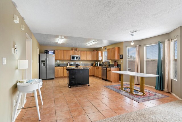 kitchen featuring pendant lighting, stainless steel appliances, a center island, a textured ceiling, and light tile patterned flooring