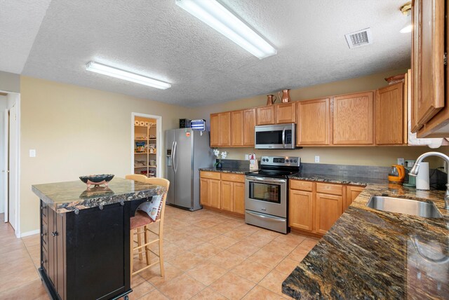 kitchen featuring a kitchen bar, sink, a textured ceiling, appliances with stainless steel finishes, and a kitchen island