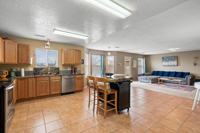 kitchen featuring light tile patterned floors, stainless steel appliances, a textured ceiling, and a kitchen bar