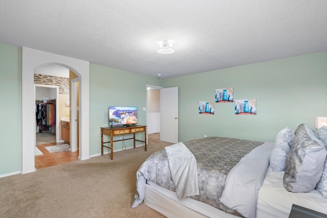 bedroom with connected bathroom, light colored carpet, and a textured ceiling