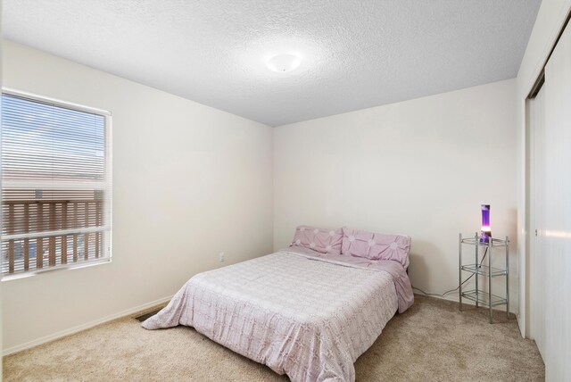 bedroom featuring multiple windows, light colored carpet, a closet, and a textured ceiling