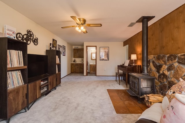 carpeted living room with wooden walls, ceiling fan, and a wood stove