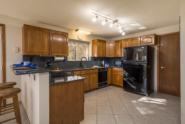 kitchen with a breakfast bar, black appliances, sink, dark stone countertops, and kitchen peninsula