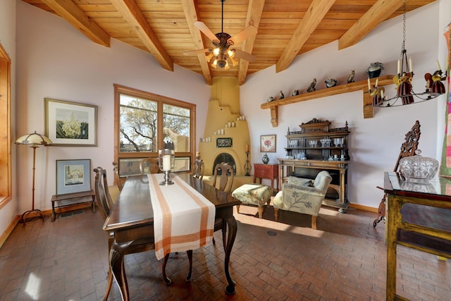 dining area featuring a fireplace, beam ceiling, ceiling fan with notable chandelier, and wooden ceiling