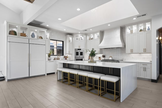 kitchen with a large island, white cabinetry, custom exhaust hood, and a kitchen breakfast bar