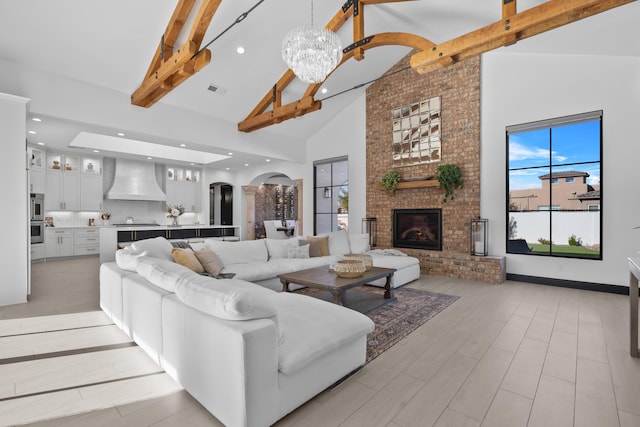 living room with high vaulted ceiling, a fireplace, beam ceiling, light hardwood / wood-style floors, and an inviting chandelier