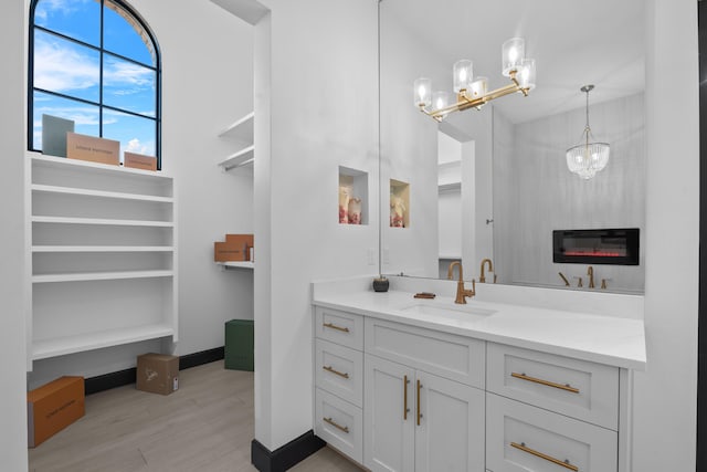 bathroom with an inviting chandelier, vanity, wood-type flooring, and a large fireplace