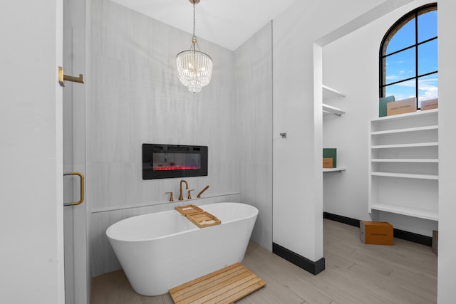 bathroom with wood-type flooring, a tub, a chandelier, and a fireplace