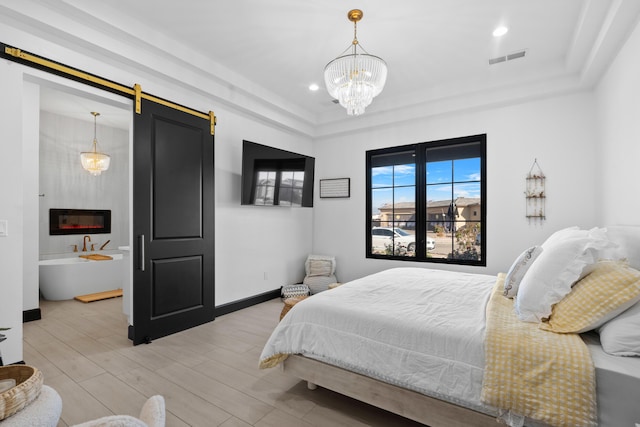 bedroom with a raised ceiling, a barn door, a notable chandelier, and light hardwood / wood-style flooring