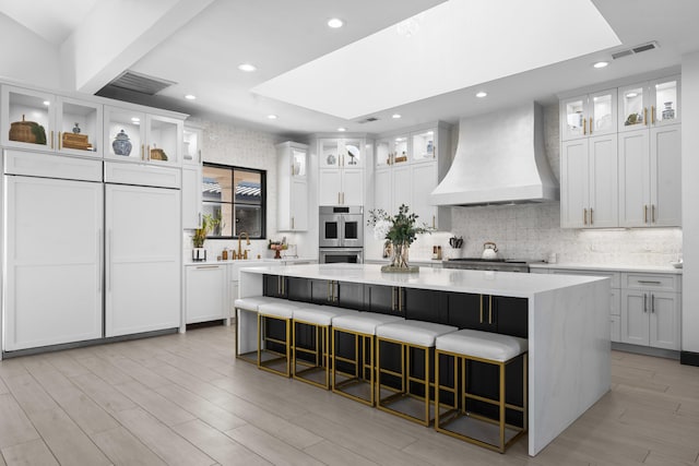 kitchen with white cabinetry, custom range hood, a breakfast bar, and a spacious island