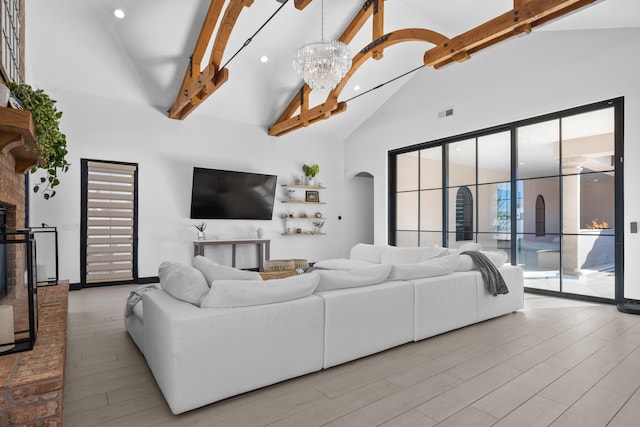 living room with beam ceiling, a brick fireplace, an inviting chandelier, and high vaulted ceiling