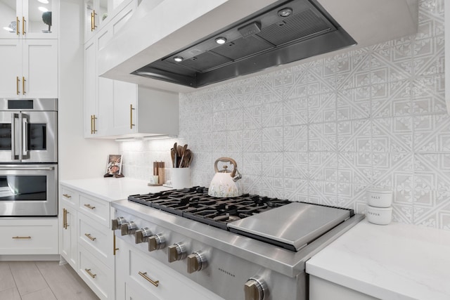 kitchen featuring decorative backsplash, appliances with stainless steel finishes, custom range hood, and white cabinets