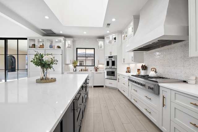 kitchen with white cabinetry, light stone countertops, custom range hood, and appliances with stainless steel finishes