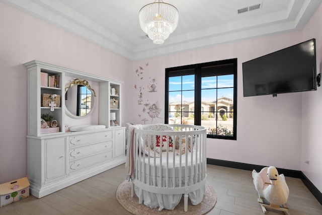 bedroom with a crib, light wood-type flooring, and a chandelier