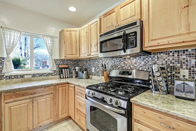 kitchen featuring light brown cabinetry, light stone countertops, backsplash, and stainless steel appliances