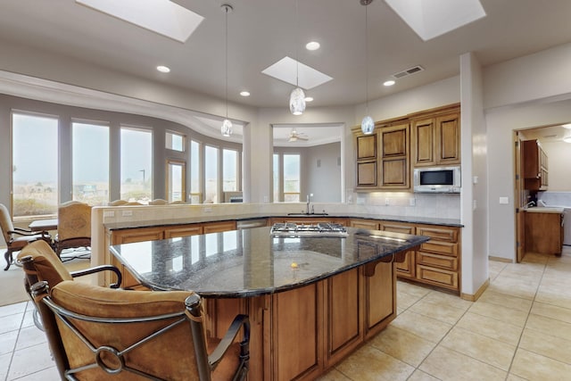 kitchen with pendant lighting, a skylight, dark stone countertops, backsplash, and stainless steel appliances