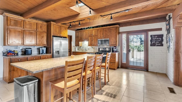 kitchen with light stone counters, tasteful backsplash, a center island, a kitchen breakfast bar, and stainless steel appliances