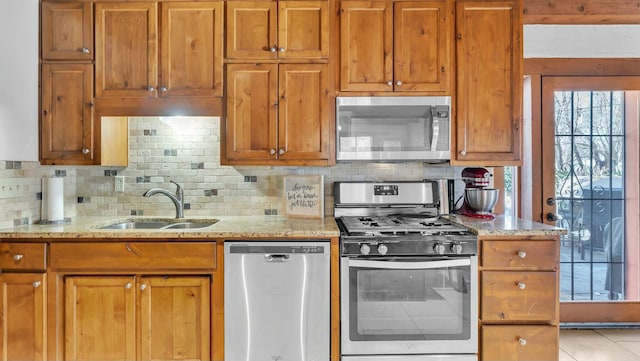 kitchen featuring stainless steel appliances, light stone countertops, sink, and backsplash