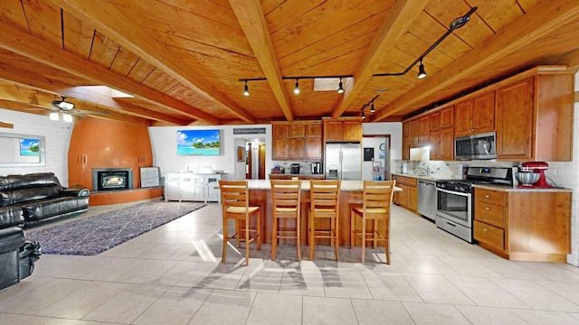 kitchen with a breakfast bar, a center island, wooden ceiling, a large fireplace, and stainless steel appliances