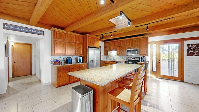 kitchen with stainless steel appliances, a center island, light stone counters, a kitchen bar, and beamed ceiling