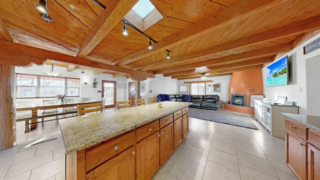 kitchen featuring a skylight, beamed ceiling, a center island, light stone countertops, and wooden ceiling