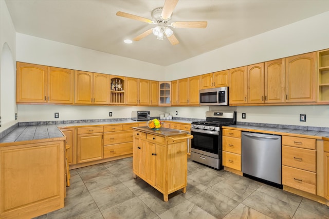 kitchen with ceiling fan, stainless steel appliances, a kitchen island, open shelves, and glass insert cabinets