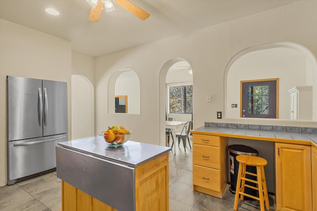 kitchen with ceiling fan, tile counters, freestanding refrigerator, and a center island