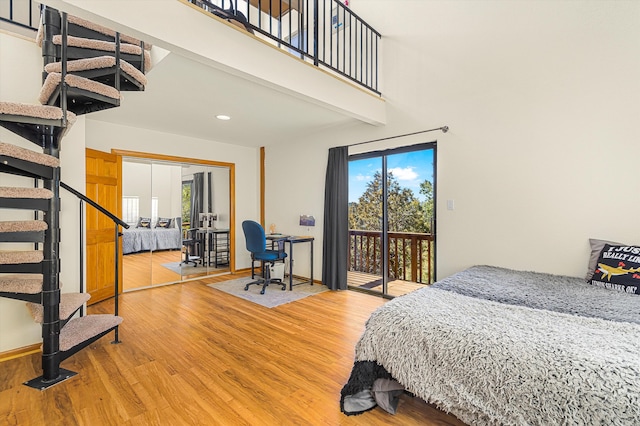 bedroom with a towering ceiling, access to exterior, baseboards, and wood finished floors