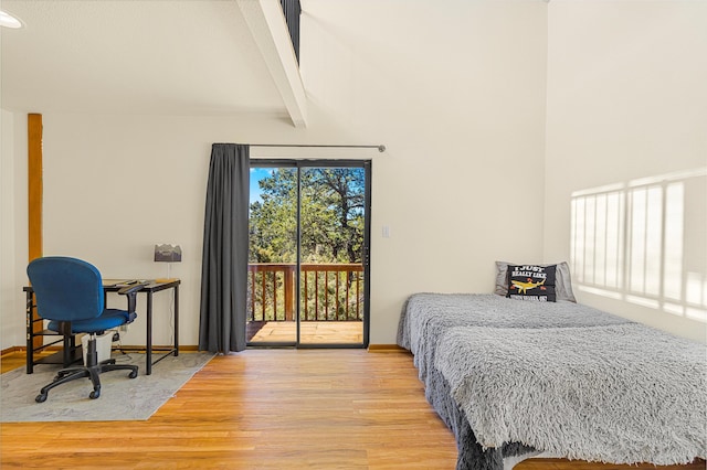 bedroom featuring baseboards, wood finished floors, beam ceiling, and access to exterior