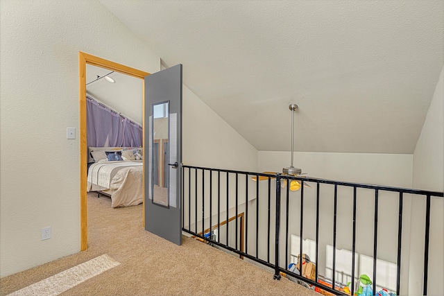 hall with vaulted ceiling, a textured ceiling, and light colored carpet