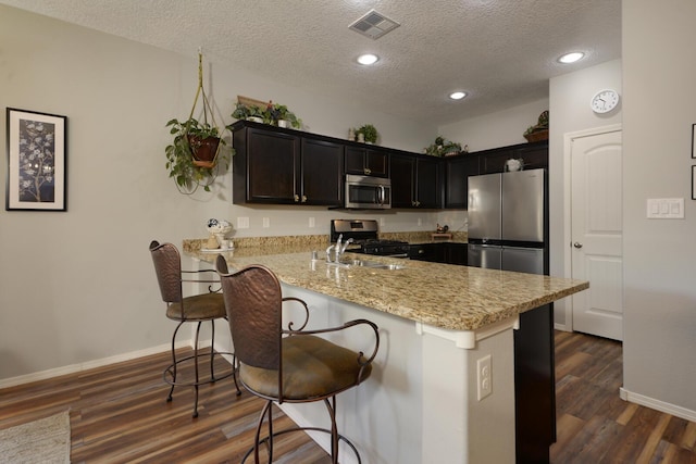 kitchen featuring a kitchen bar, sink, dark hardwood / wood-style floors, stainless steel appliances, and light stone countertops