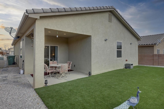 back house at dusk featuring a patio area and a lawn