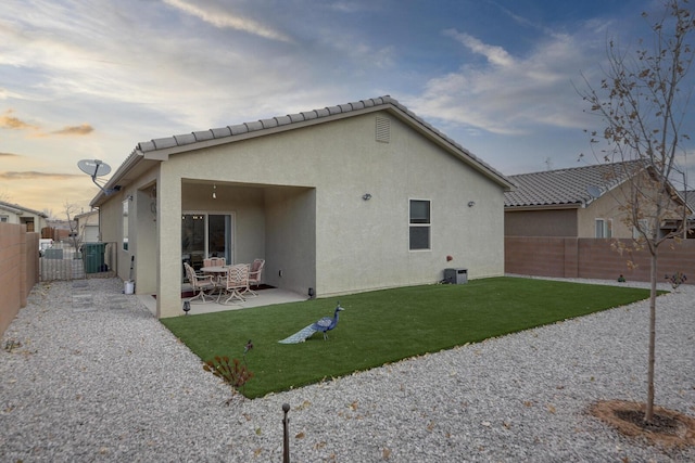 back house at dusk featuring a yard and a patio area