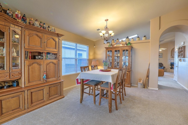 dining space with ceiling fan with notable chandelier, vaulted ceiling, and light colored carpet