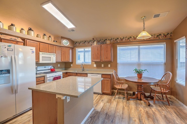 kitchen featuring sink, light wood-type flooring, hanging light fixtures, a center island, and white appliances