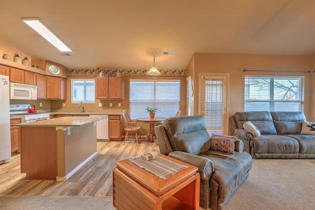 kitchen featuring sink, white appliances, a kitchen island, decorative light fixtures, and light wood-type flooring