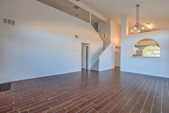 unfurnished living room with dark wood-type flooring, a notable chandelier, and high vaulted ceiling