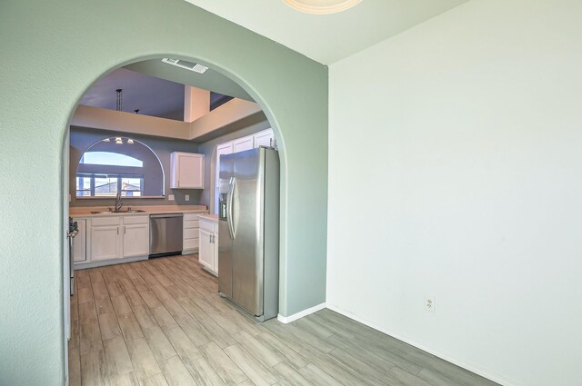 kitchen with light wood-type flooring, stainless steel appliances, sink, and white cabinets