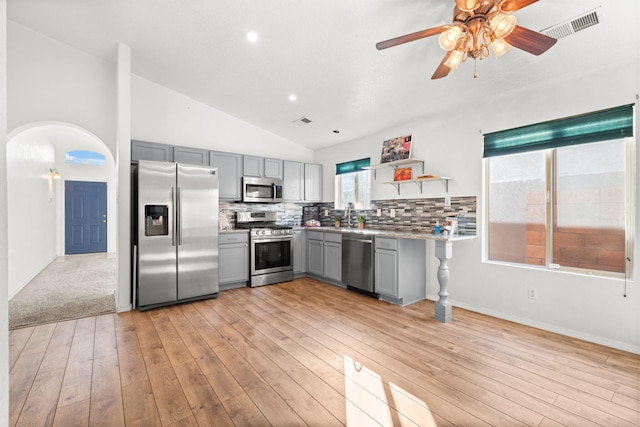 kitchen with gray cabinetry, stainless steel appliances, a sink, light countertops, and open shelves