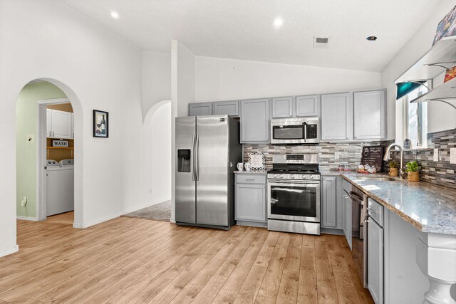 kitchen featuring lofted ceiling, light stone countertops, stainless steel appliances, washing machine and dryer, and a sink