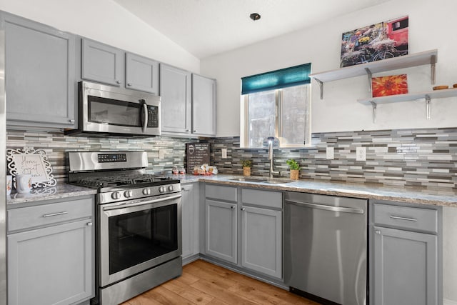 kitchen featuring a sink, stainless steel appliances, gray cabinets, and light stone countertops