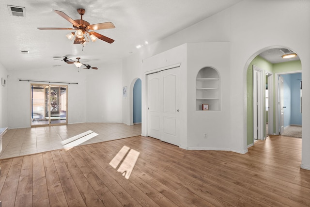 interior space with arched walkways, built in shelves, and light wood-style floors