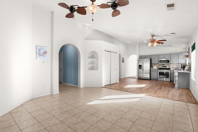 kitchen featuring arched walkways, light countertops, appliances with stainless steel finishes, and gray cabinetry