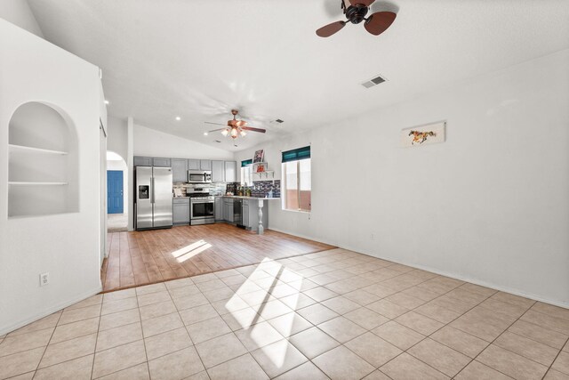 unfurnished living room with ceiling fan, light tile patterned floors, vaulted ceiling, and visible vents