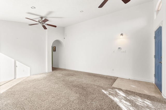 unfurnished living room with a ceiling fan, arched walkways, and carpet flooring