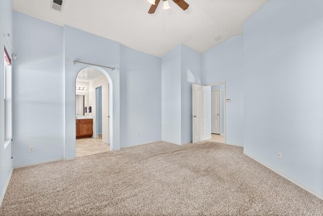 unfurnished bedroom featuring arched walkways, visible vents, light carpet, connected bathroom, and high vaulted ceiling