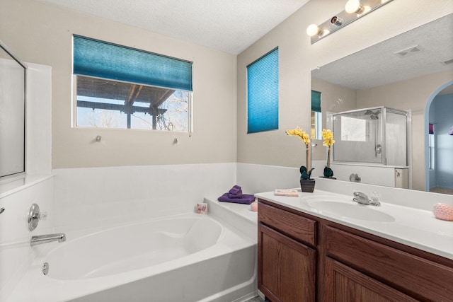 full bathroom with a textured ceiling, a garden tub, vanity, visible vents, and a shower stall