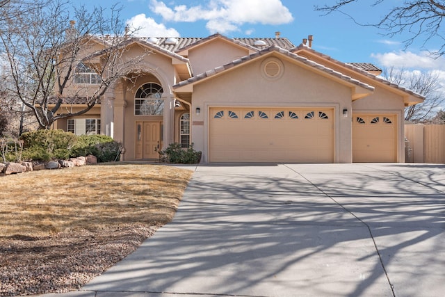 mediterranean / spanish house with an attached garage, a tiled roof, concrete driveway, and stucco siding