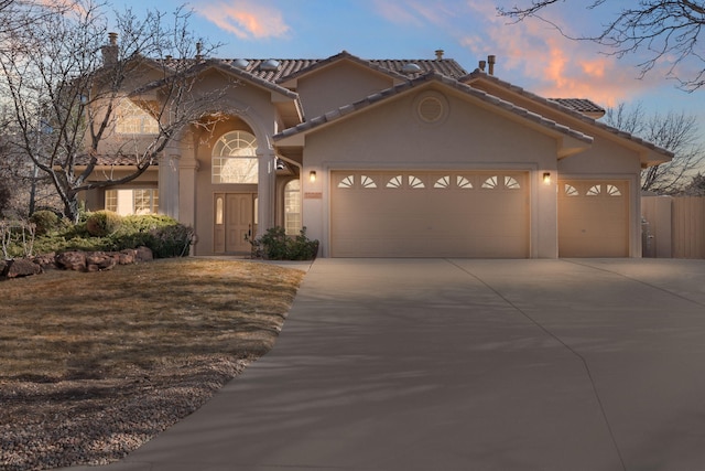 mediterranean / spanish house with a garage, concrete driveway, a tiled roof, and stucco siding