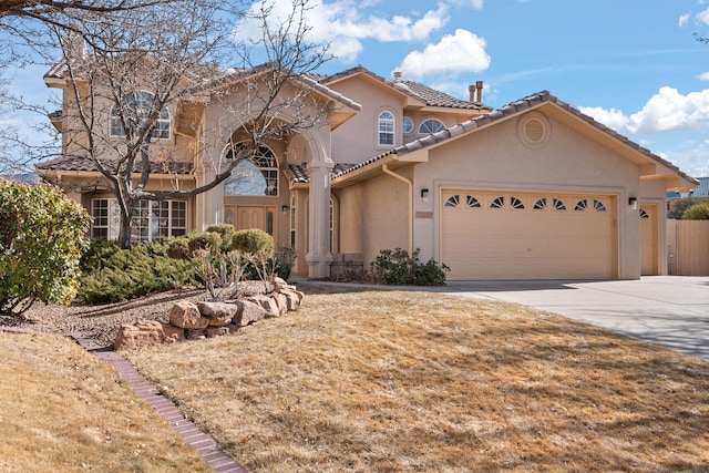 mediterranean / spanish house with driveway, an attached garage, a tiled roof, and stucco siding